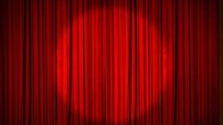 A red stage curtain, drawn, with a circular spotlight shining on the middle of it.